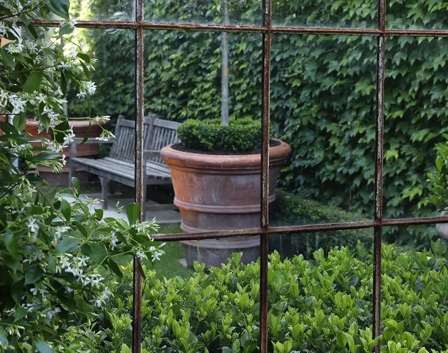 A grid-style window looking out onto a garden with a large terracotta pot and wooden bench.