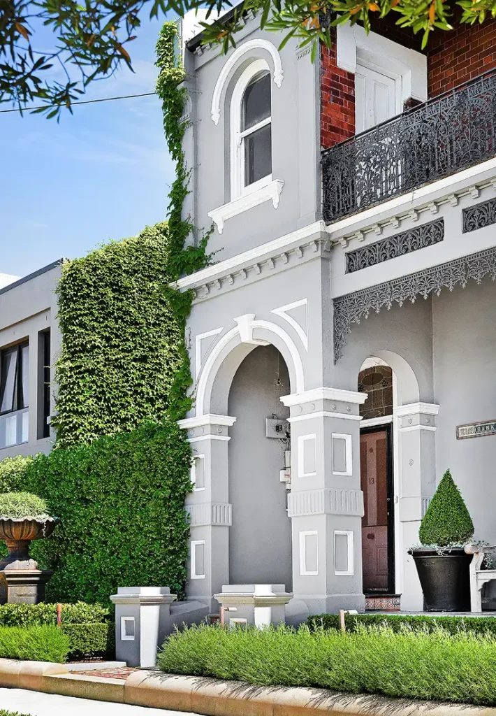 The exterior of a grand grey two-story house with white trim, balconies, and climbing ivy.
